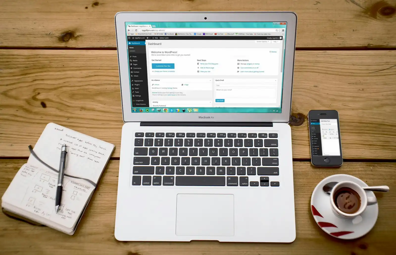Laptop with CMS interface open on wooden desk next to notebook and coffee