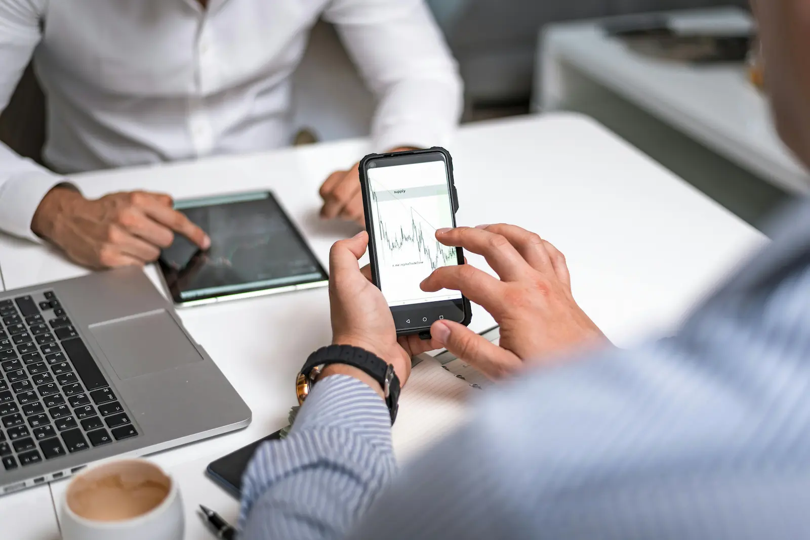 Business professional reviewing mobile analytics data on smartphone beside a laptop at desk